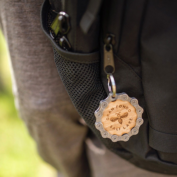 Gran Fondo Salt Lake bamboo keychain clipped to a rider's backpack on the trail